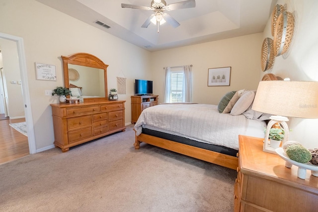 carpeted bedroom featuring ceiling fan and a raised ceiling