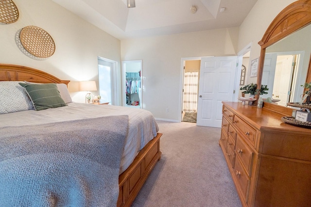 carpeted bedroom featuring a tray ceiling, a spacious closet, a closet, and ensuite bathroom