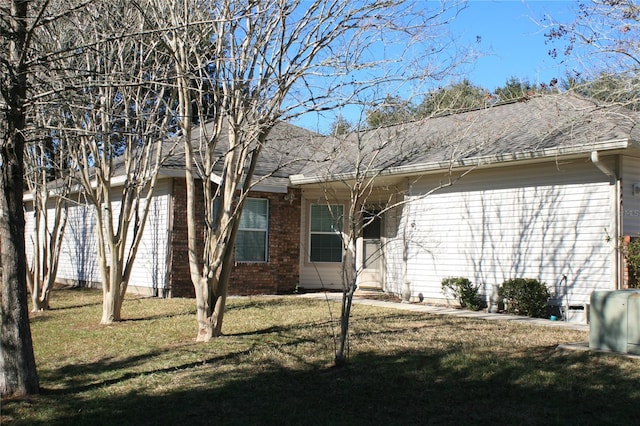 exterior space with brick siding, roof with shingles, and a yard