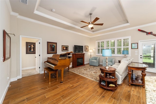 living room with wood-type flooring, a healthy amount of sunlight, ornamental molding, and a tray ceiling