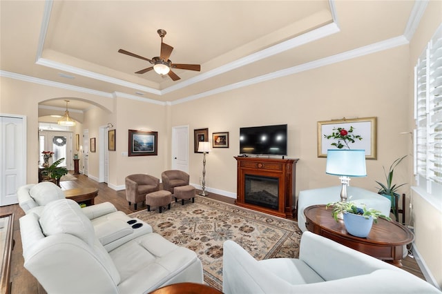 living room with crown molding, hardwood / wood-style flooring, a raised ceiling, and ceiling fan