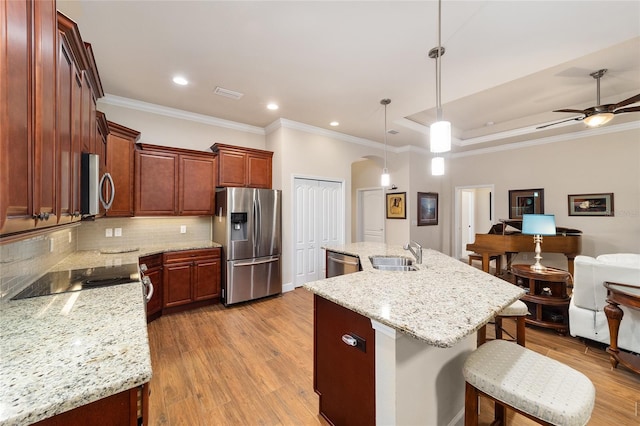 kitchen featuring sink, light wood-type flooring, pendant lighting, stainless steel appliances, and a kitchen island with sink