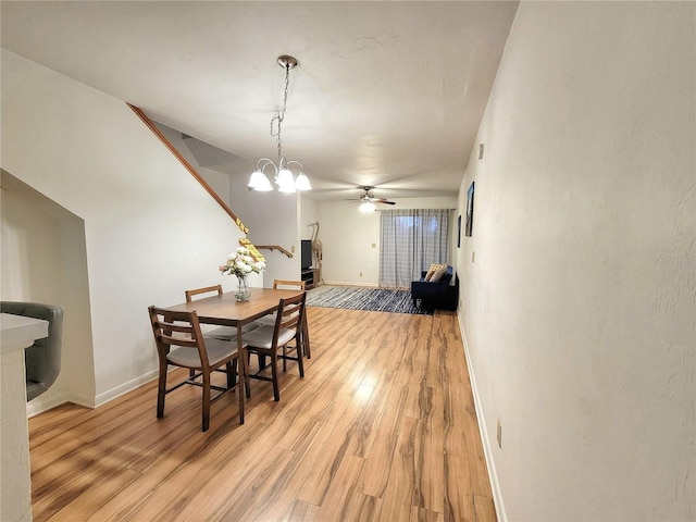 dining space with ceiling fan with notable chandelier and light hardwood / wood-style floors