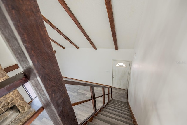 staircase featuring vaulted ceiling with beams and a stone fireplace