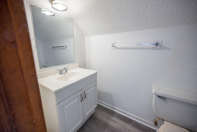 bathroom with vanity, a textured ceiling, vaulted ceiling, wood-type flooring, and toilet