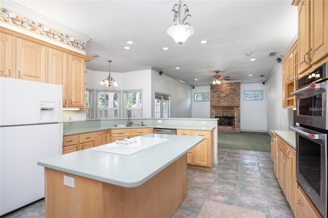 kitchen with light brown cabinets, a brick fireplace, pendant lighting, a kitchen island, and appliances with stainless steel finishes