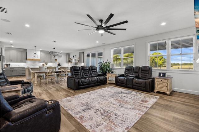 living room featuring ceiling fan with notable chandelier and light hardwood / wood-style flooring