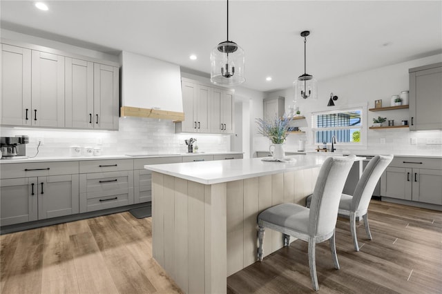 kitchen with hanging light fixtures, light hardwood / wood-style floors, gray cabinets, and premium range hood