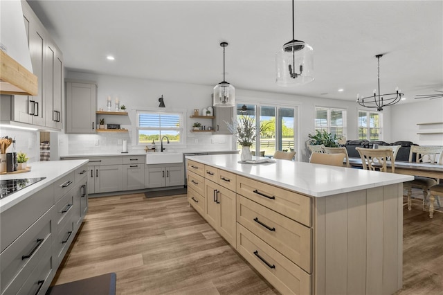 kitchen with decorative backsplash, custom range hood, pendant lighting, gray cabinets, and a kitchen island