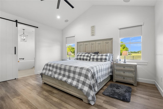 bedroom with high vaulted ceiling, ensuite bath, ceiling fan, a barn door, and light wood-type flooring