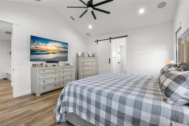 bedroom with ceiling fan, a barn door, light hardwood / wood-style floors, and vaulted ceiling