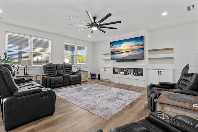 living room featuring a large fireplace, light hardwood / wood-style flooring, and ceiling fan