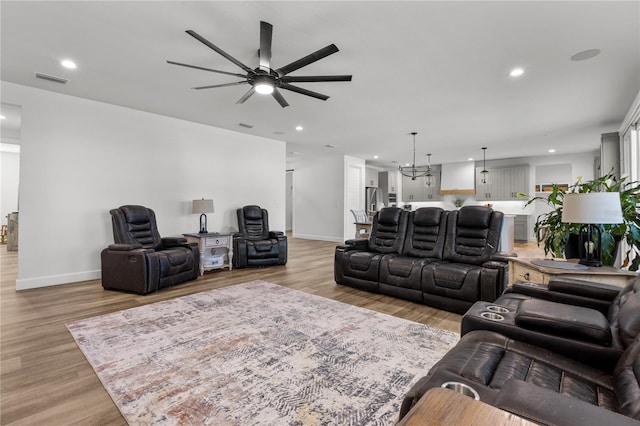 living room featuring ceiling fan with notable chandelier and light wood-type flooring