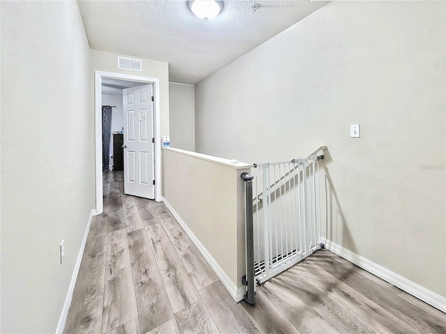 corridor with a textured ceiling and light wood-type flooring