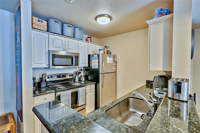 kitchen with sink, white cabinetry, appliances with stainless steel finishes, and dark stone counters