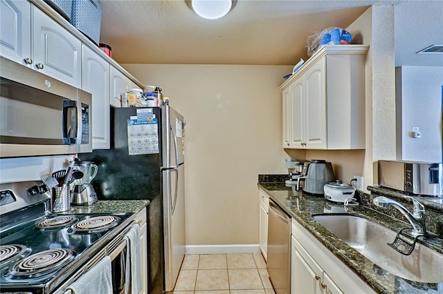 kitchen with dark stone countertops, sink, light tile patterned floors, stainless steel appliances, and white cabinets