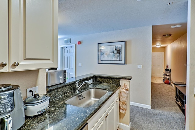 kitchen featuring sink, white cabinetry, dark stone counters, and carpet flooring