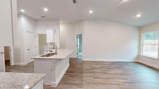 kitchen with sink, white cabinetry, light stone counters, wood-type flooring, and a center island with sink