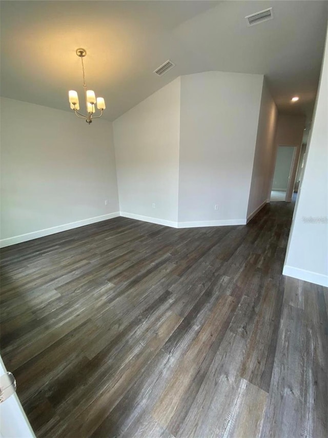 spare room with dark hardwood / wood-style flooring and an inviting chandelier