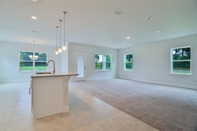 kitchen with pendant lighting, sink, a kitchen island with sink, light carpet, and light stone counters