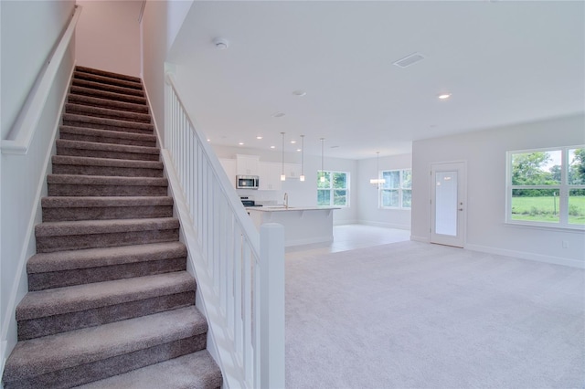 stairway with carpet, a chandelier, and sink