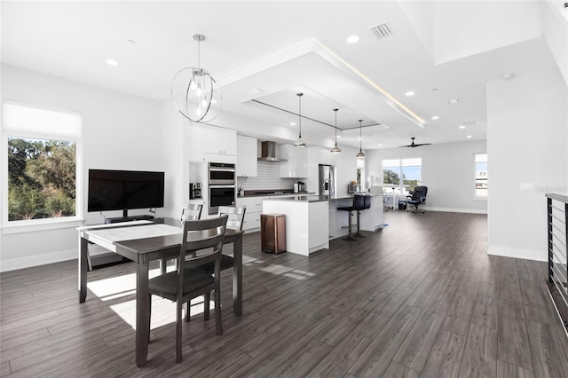 dining room with a raised ceiling, ceiling fan, and dark wood-type flooring