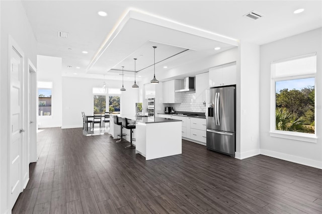 kitchen featuring a kitchen breakfast bar, stainless steel appliances, white cabinetry, hanging light fixtures, and an island with sink