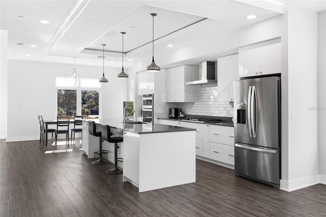 kitchen with wall chimney exhaust hood, a raised ceiling, white cabinetry, and appliances with stainless steel finishes