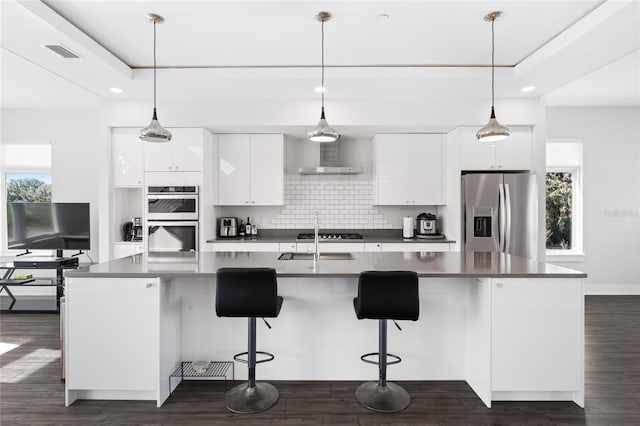 kitchen with stainless steel appliances, a raised ceiling, decorative light fixtures, a center island with sink, and white cabinets