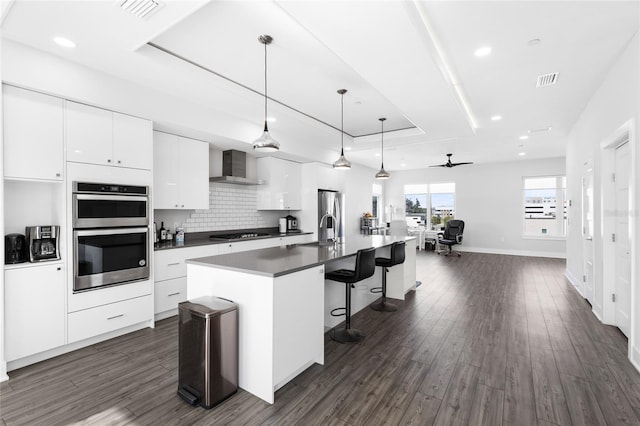 kitchen featuring a tray ceiling, ceiling fan, a center island with sink, and white cabinetry