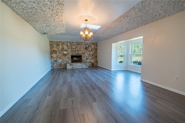 unfurnished living room featuring lofted ceiling, dark hardwood / wood-style floors, a stone fireplace, and a notable chandelier