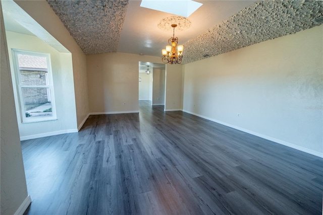 spare room with ceiling fan with notable chandelier, lofted ceiling with skylight, and dark wood-type flooring