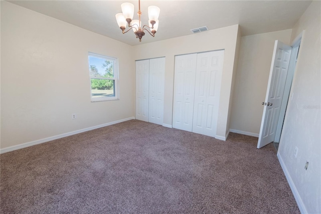 unfurnished bedroom with carpet flooring, two closets, and a notable chandelier