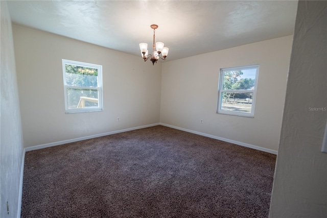 empty room with dark carpet and an inviting chandelier