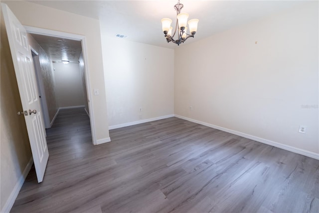 empty room with hardwood / wood-style flooring and an inviting chandelier