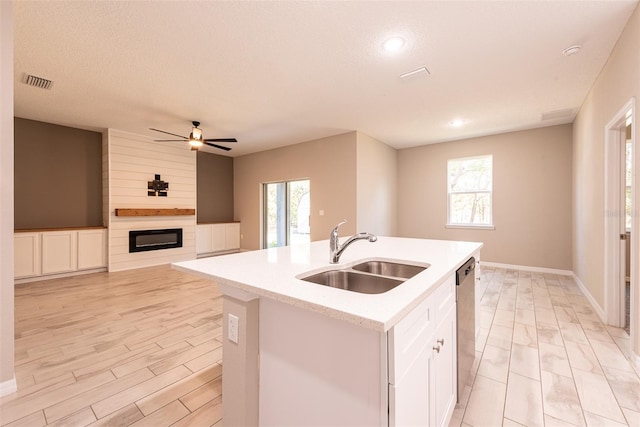 kitchen with ceiling fan, a large fireplace, sink, stainless steel dishwasher, and an island with sink