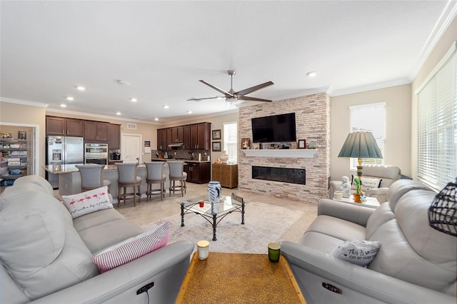 living room featuring crown molding, ceiling fan, plenty of natural light, and a stone fireplace