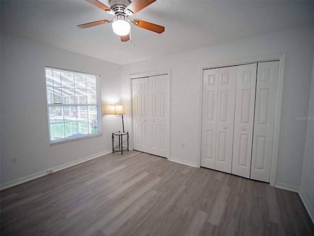 unfurnished bedroom featuring ceiling fan, light hardwood / wood-style floors, and two closets