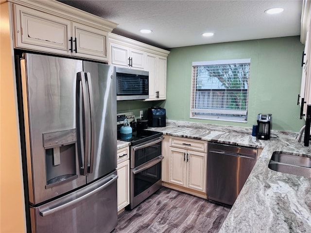 kitchen featuring appliances with stainless steel finishes, light stone counters, a textured ceiling, sink, and cream cabinetry