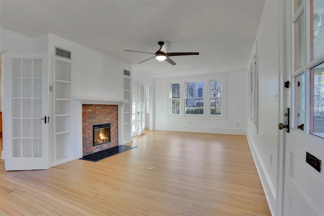 unfurnished living room with french doors, ceiling fan, light hardwood / wood-style flooring, built in features, and a fireplace