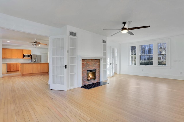 unfurnished living room featuring french doors, light hardwood / wood-style floors, a brick fireplace, and ceiling fan