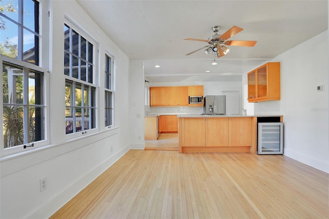 kitchen with kitchen peninsula, appliances with stainless steel finishes, beverage cooler, ceiling fan, and light hardwood / wood-style flooring