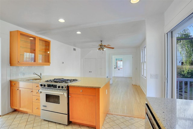 kitchen with backsplash, light stone counters, ceiling fan, sink, and high end stainless steel range