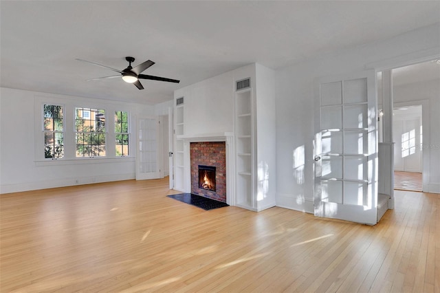 unfurnished living room featuring ceiling fan, built in features, light wood-type flooring, and a brick fireplace