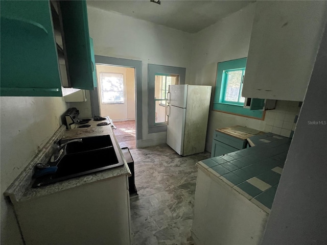 kitchen featuring white refrigerator, a healthy amount of sunlight, tile countertops, and sink