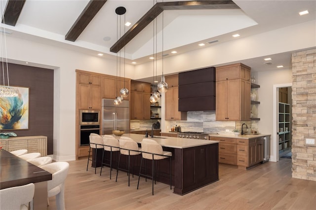 kitchen featuring built in appliances, wall chimney range hood, hanging light fixtures, and beam ceiling