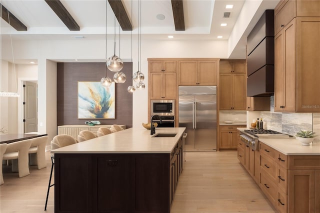 kitchen with sink, built in appliances, wall chimney exhaust hood, a center island with sink, and a breakfast bar