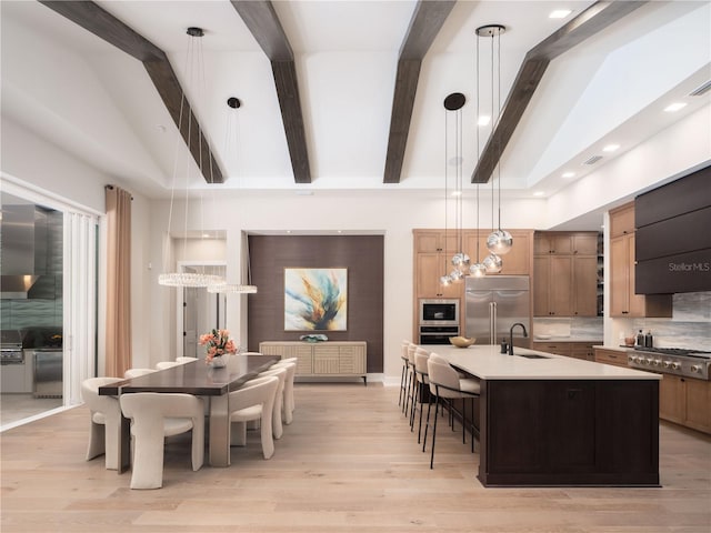 kitchen with decorative light fixtures, a kitchen island with sink, built in appliances, and sink