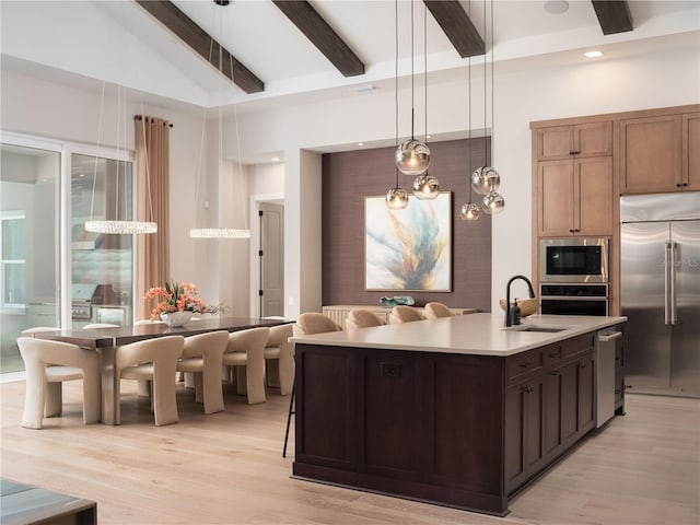 kitchen with a kitchen island with sink, built in appliances, beamed ceiling, sink, and decorative light fixtures