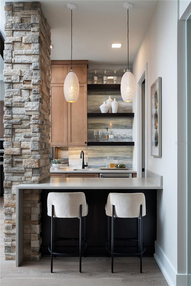 bar featuring sink, hanging light fixtures, and light hardwood / wood-style flooring